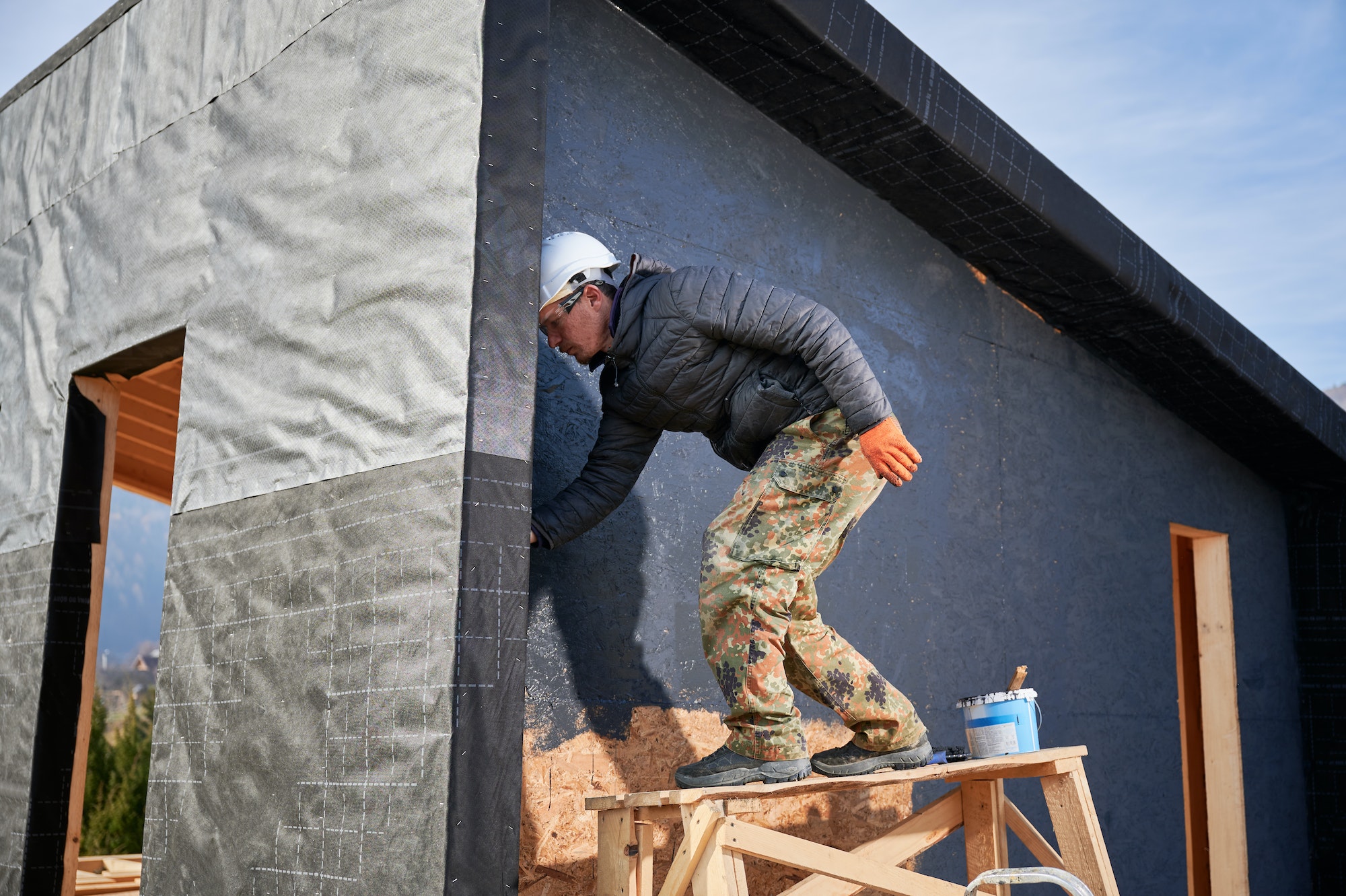 Male painter using paint roller, doing exterior paint work while building wooden frame house.