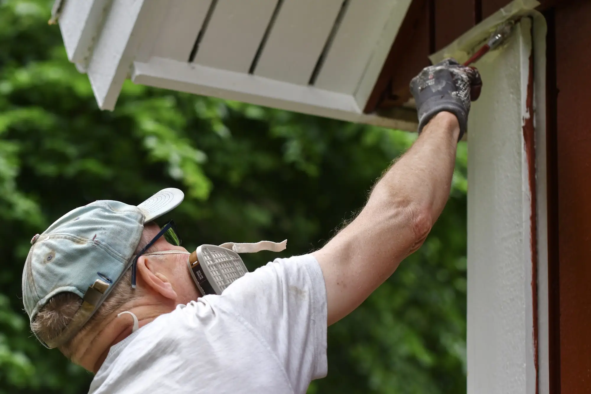 Close-up of exterior painting in South King County showing a worker painting house trim near the roofline.