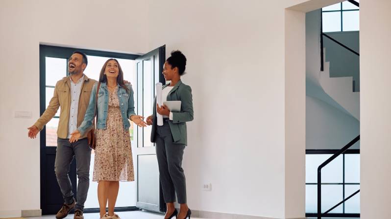 Couple touring a modern home with a realtor, showcasing completed spec unit renovations in a bright, open living space.