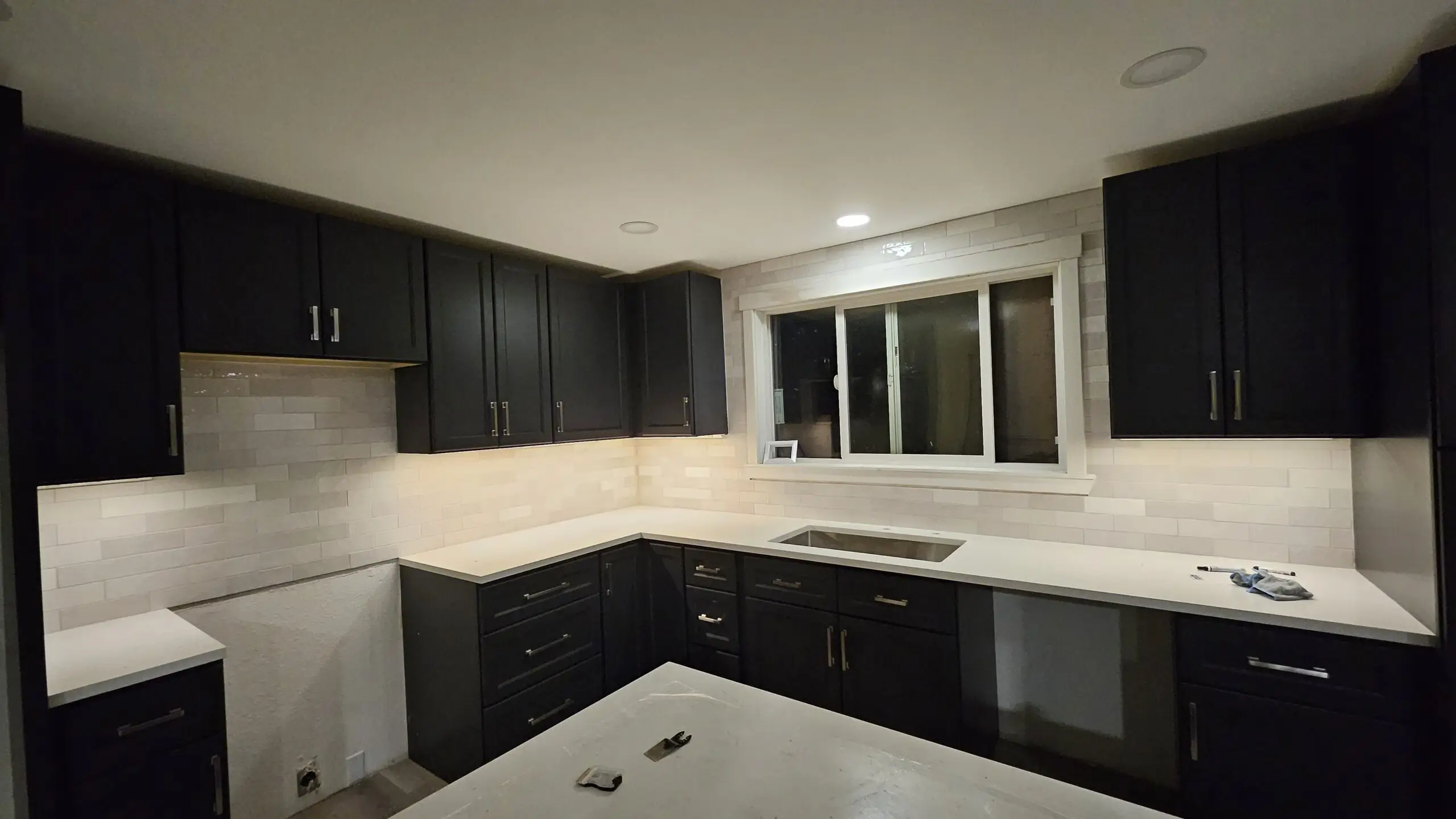 Sleek kitchen remodel in South King County featuring dark cabinetry and light tile walls.