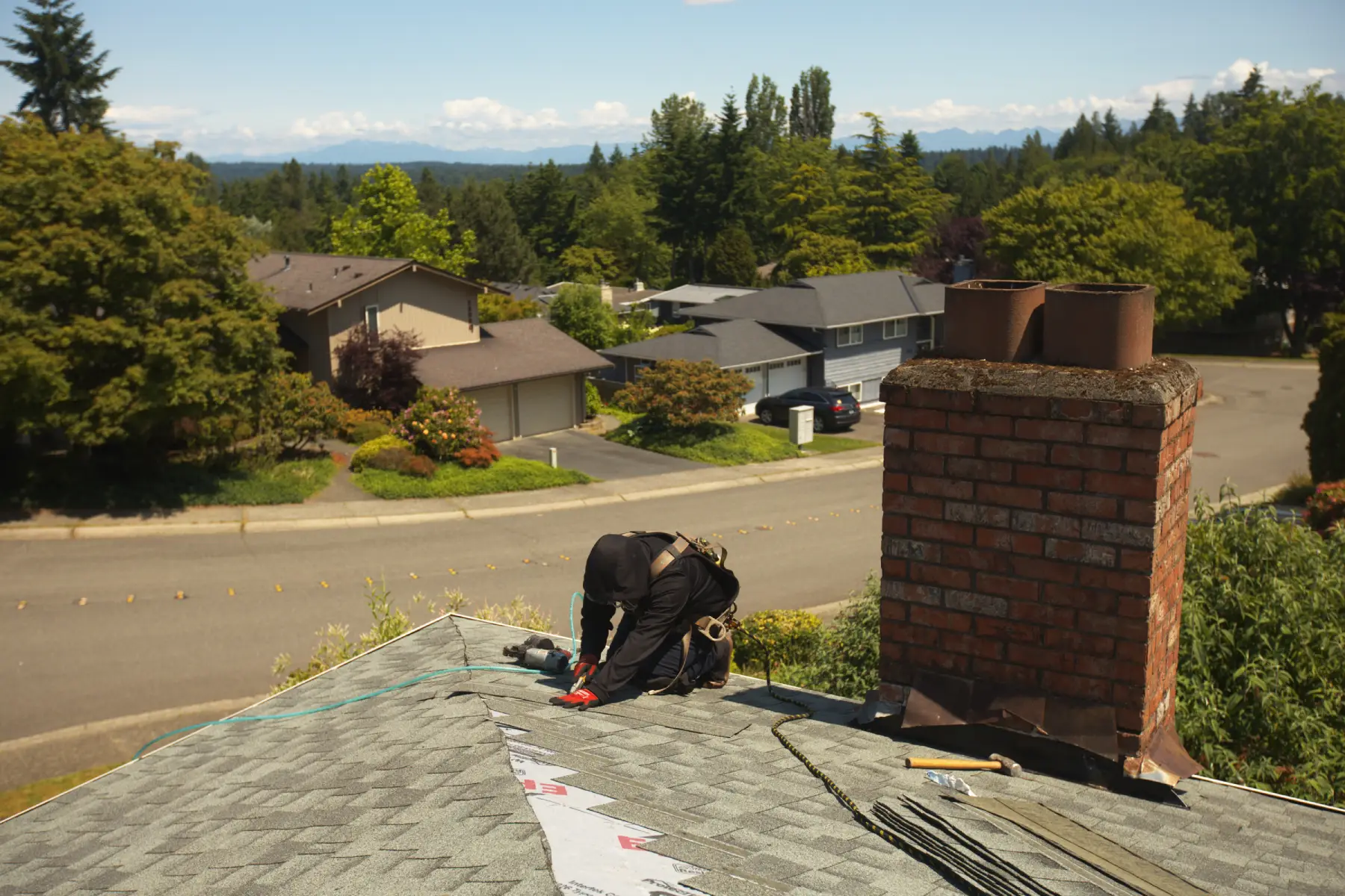 Roofer performing roof maintenance services on shingles near a chimney in a quiet residential neighborhood.