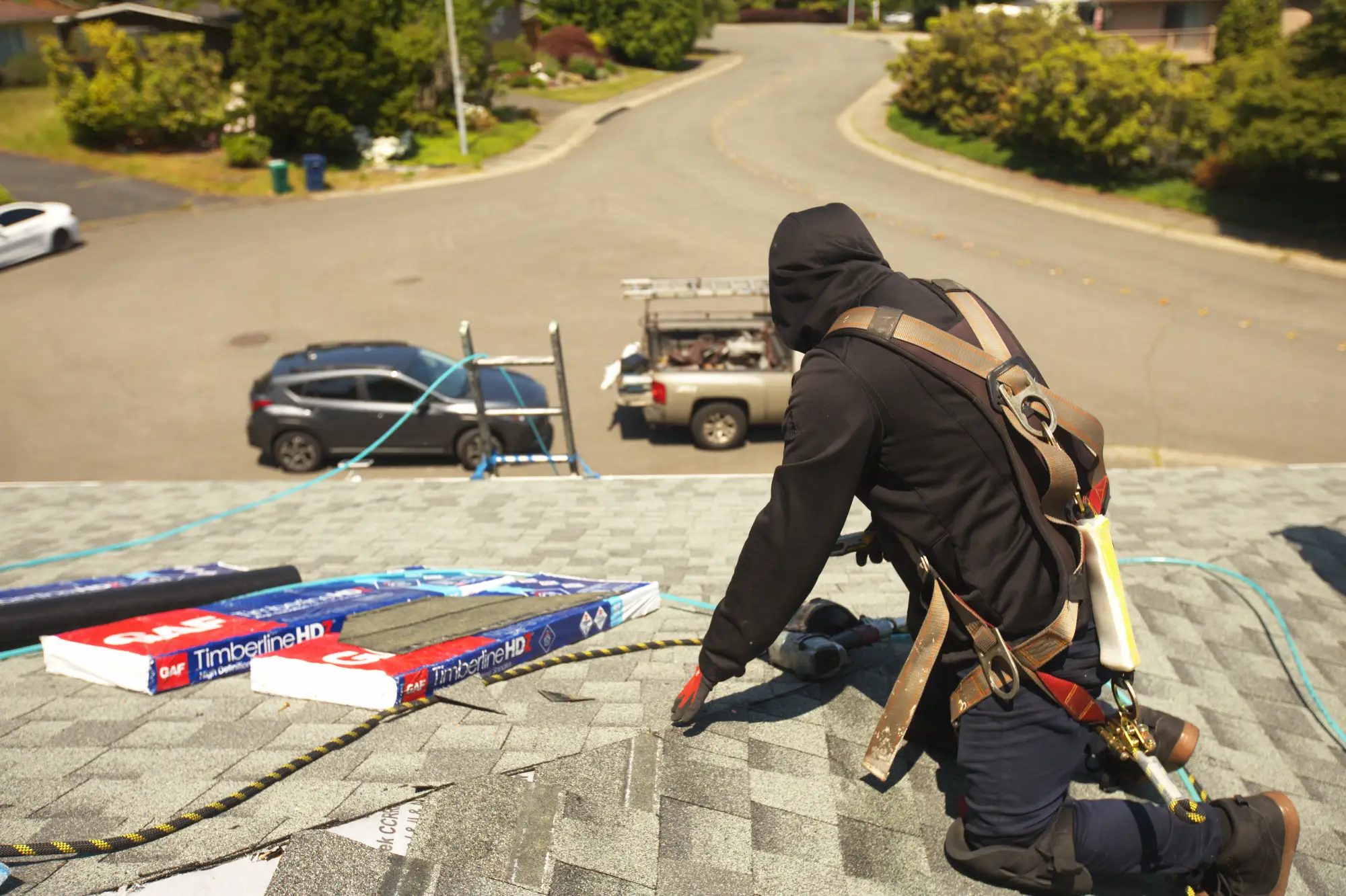 Contractor working on shingles for roof repair services, using safety gear and tools on a sunny day.