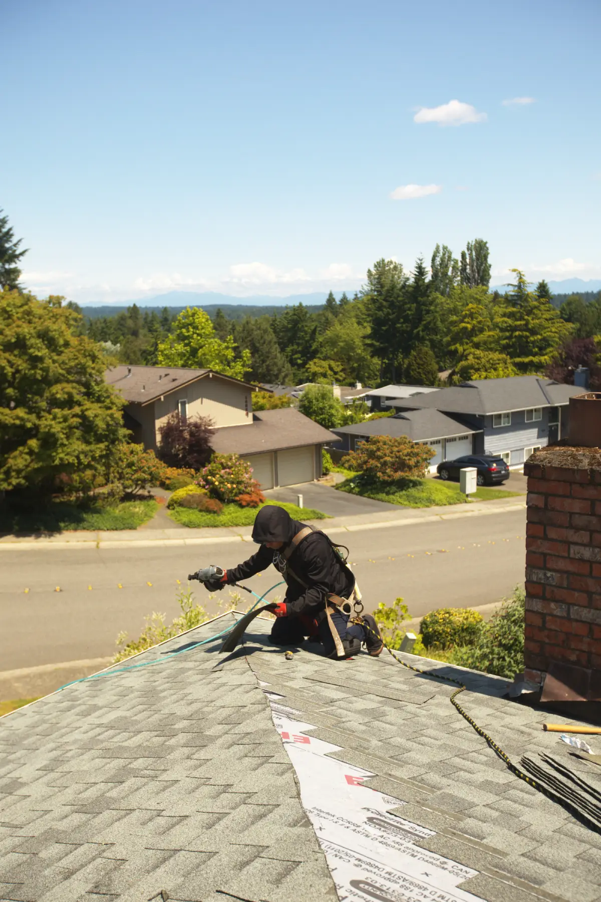 Roofing contractor working on shingles, providing trusted roofing repair services for neighborhood homes on a clear day.